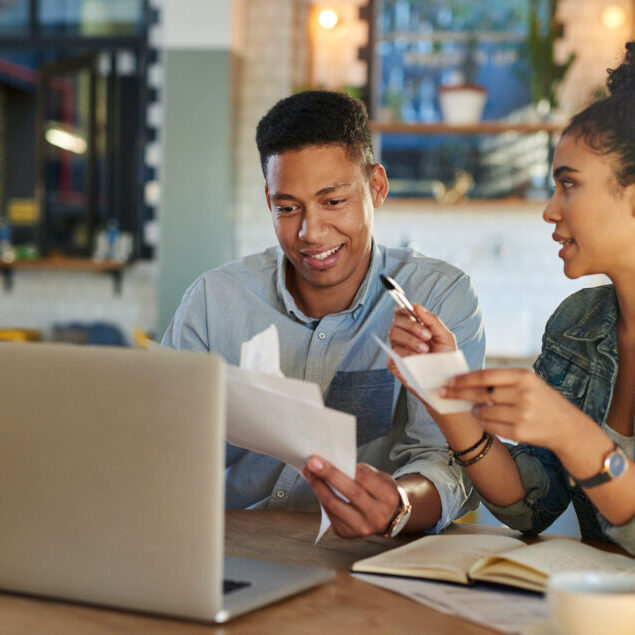 Cropped shot of two young cafe owners sitting in a coffee shop with a laptop to discuss their financial paperwork