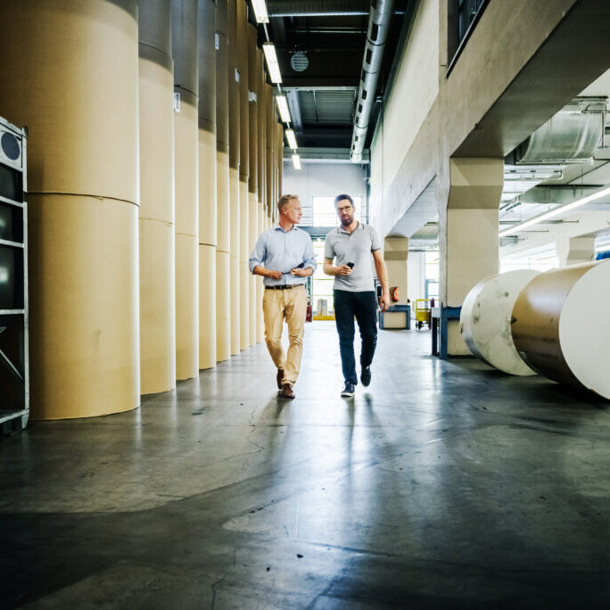 Engineer and manager walking and talking in a large paper roll storagehouse of a printery