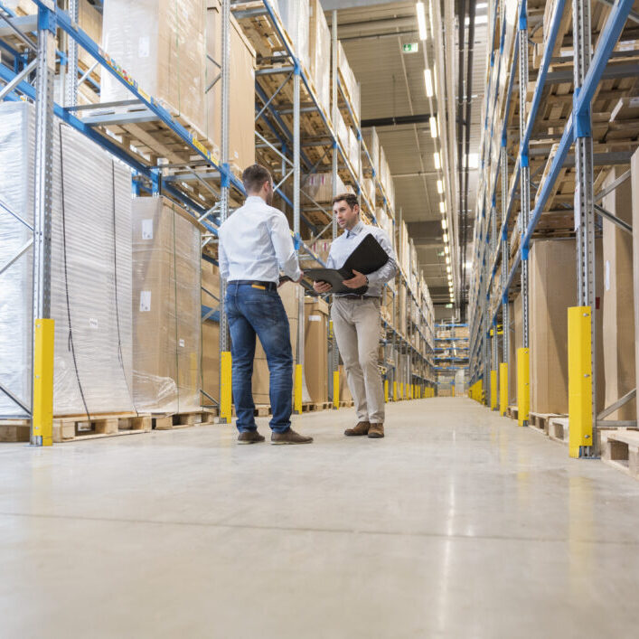 Two men with folder talking in factory warehouse